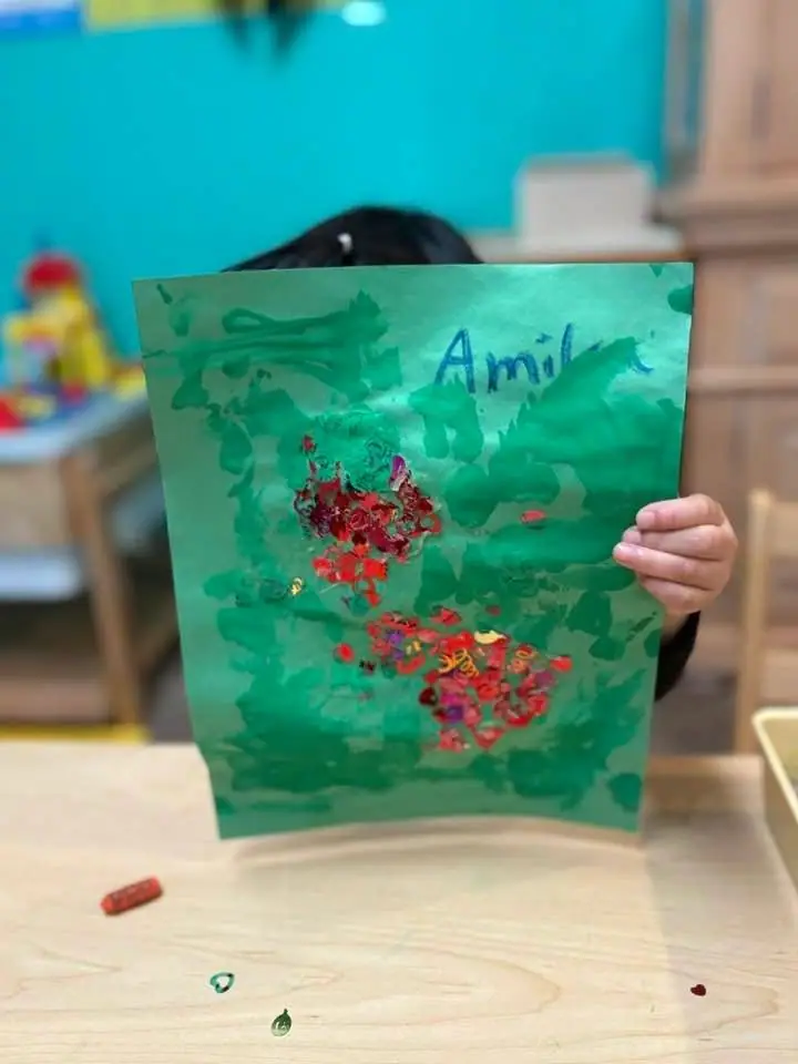 A child holding up a green painting dotted with red paint