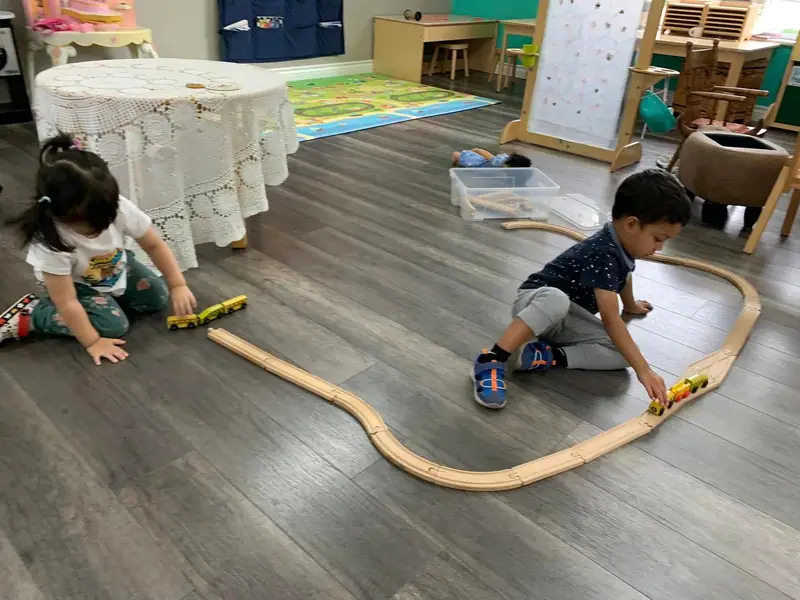 A child laying out a curved wooden train track across the classroom floor