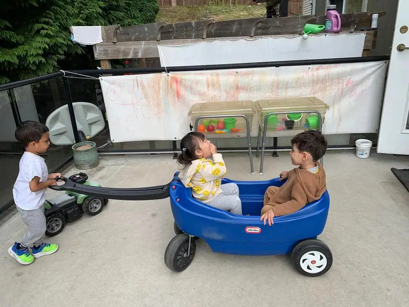 Two toddlers sitting together in a blue wagon on the covered deck