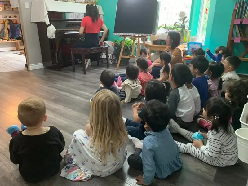 Children sitting on the floor listening to an educator play the piano during circle time