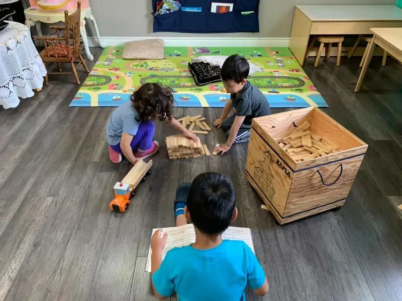 Children playing with wooden blocks and a picture book on the road-map rug
