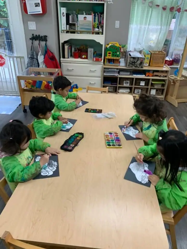 Children painting at the long table in green art smocks