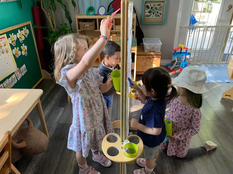 A child reaching up to a hanging water activity while others play nearby