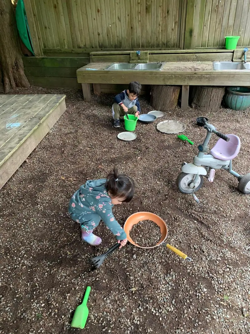 Two children digging with buckets and sieves in the outdoor sand pit