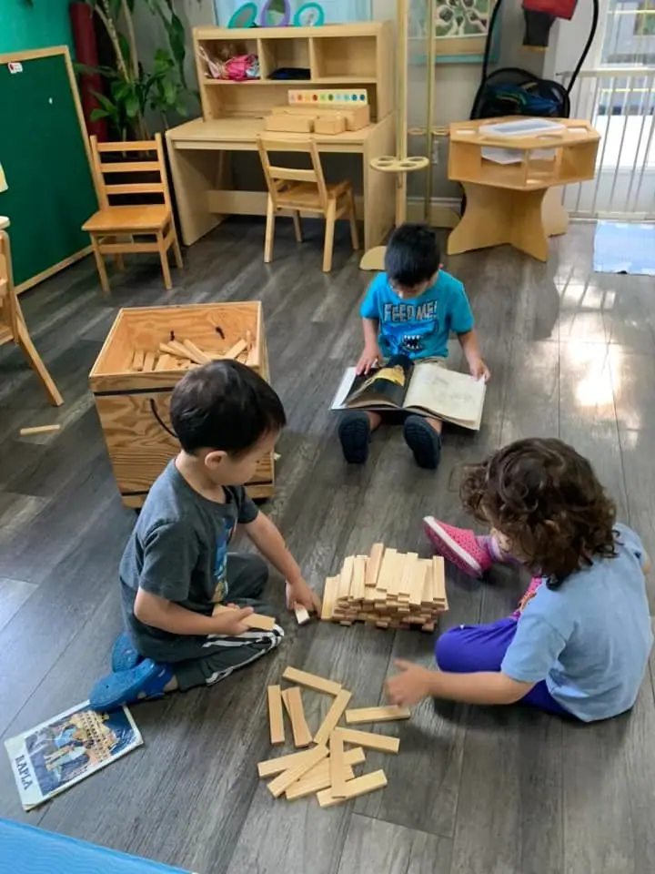 Children reading a book together and building with wooden planks on the floor