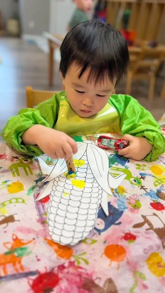 A toddler in a green smock colouring a picture at a table