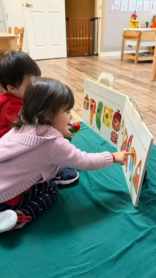A toddler pointing at a picture board of the very hungry caterpillar