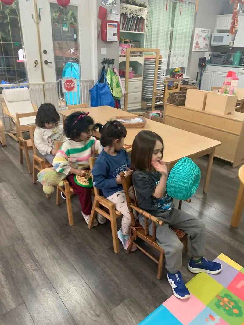 Children seated in a row of little wooden chairs at the table