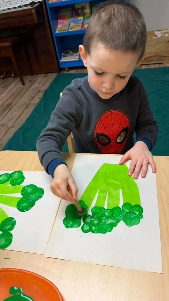 A child pressing green paint handprints onto paper