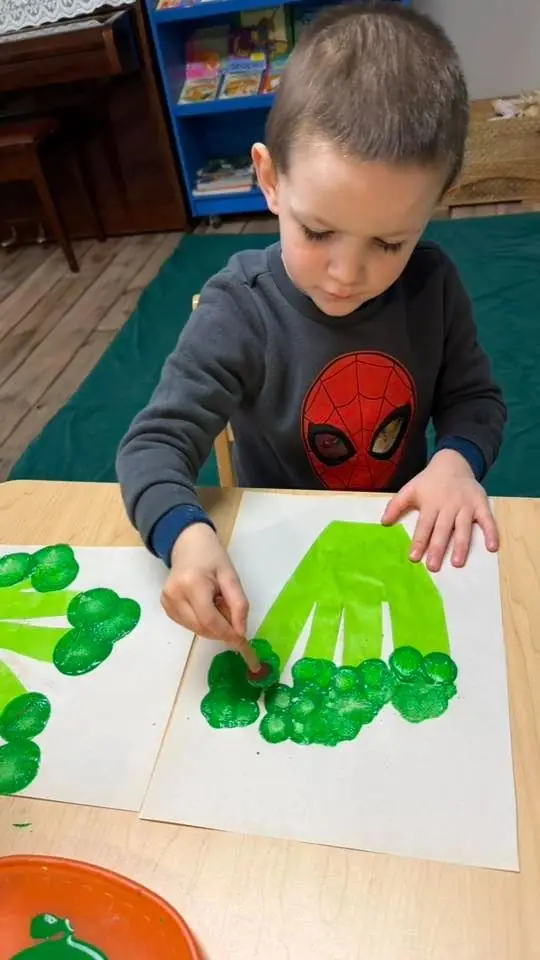 A child pressing green paint handprints onto paper