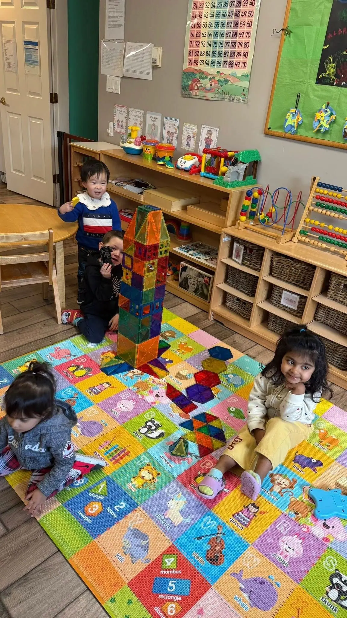 Children building with magnetic tiles beside the shelves