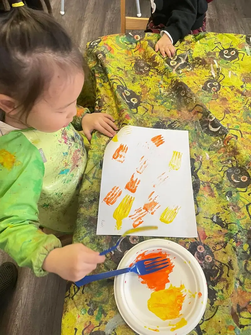A toddler stamping orange handprints onto paper