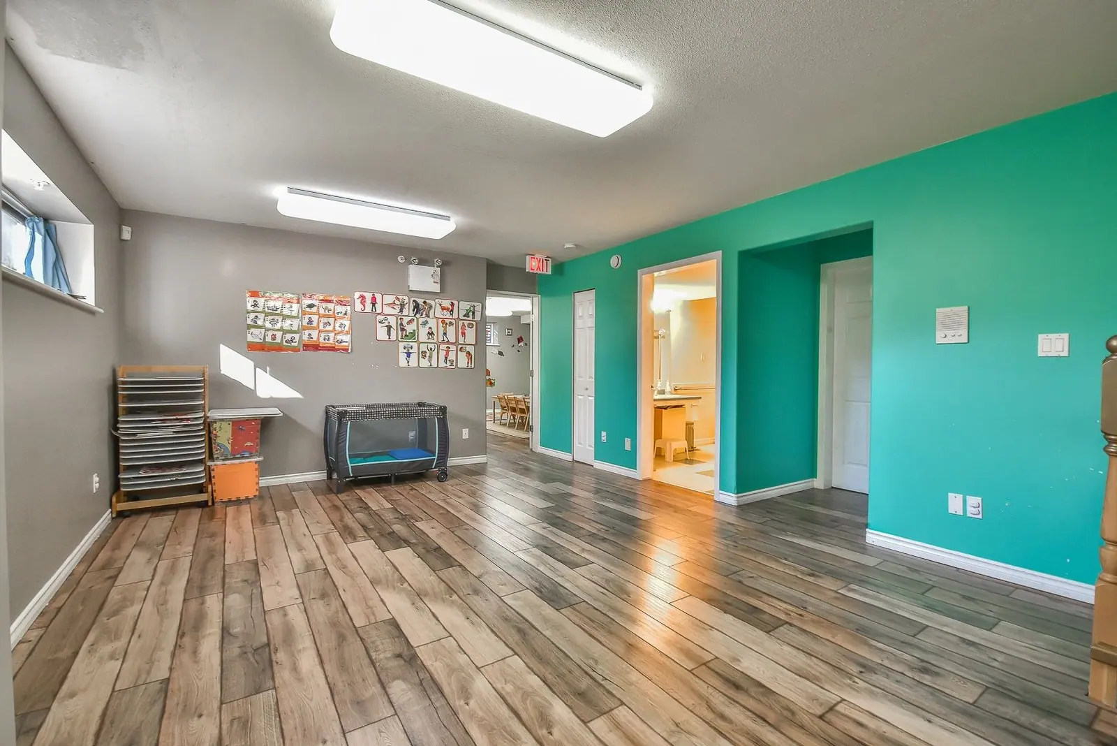 An open room with wood floors leading through to a teal doorway